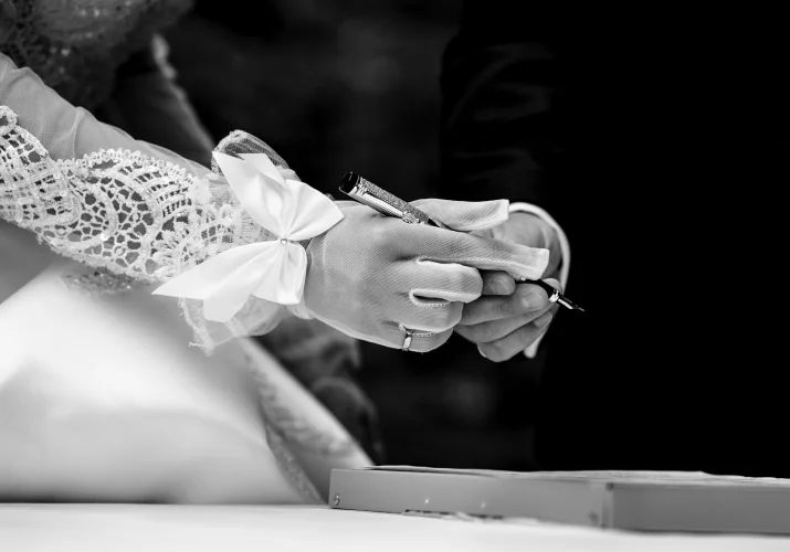 Black and white photograph of newlyweds hands. Bride passing a pen to the groom.