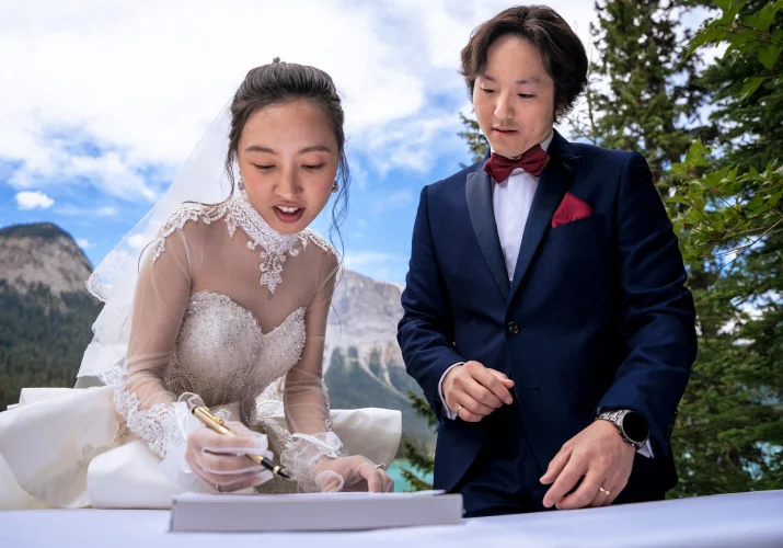 The bride sighs the official papers while the groom watches her.