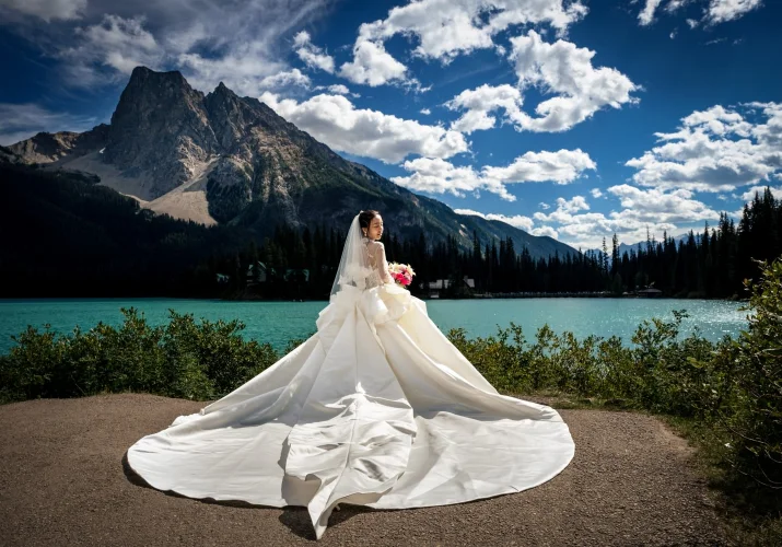 Bride wearing a huge , white wedding dress by the turquoise Emerald Lake.