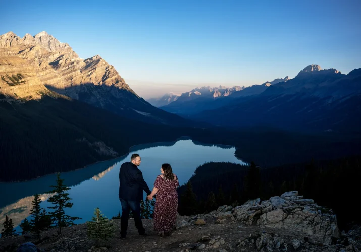 engaged couple hold their hands and look at each other on the top of the mountain at Peyto Lake in Banff.