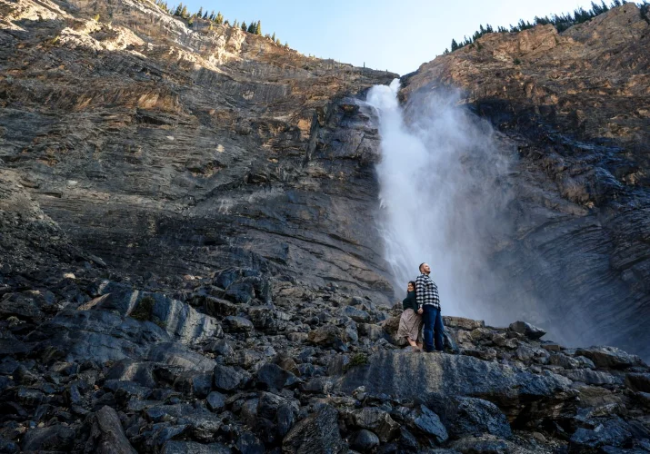 Man and lady stand back to back . Behind them powerful waterfall in Banff.