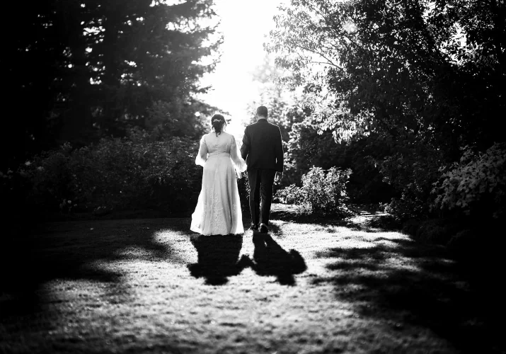 Black and white photograph of bride and groom walking at Calgary Zoo park. They walk away towards the sun which gives interesting shadows.