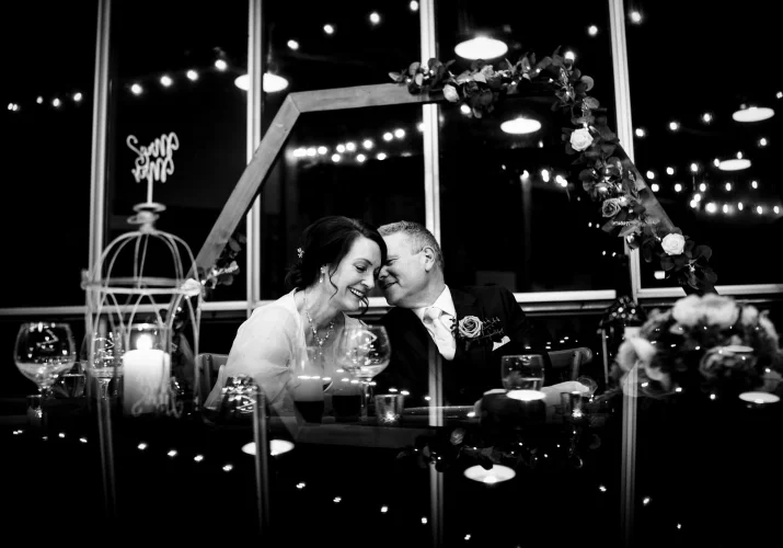 Groom share a secret with his wife during the reception. Photography in black and white with amazong reflaction.