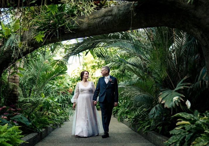 Newlyweds walk in the Calgary Zoo garden, holding hands and looking at each other.