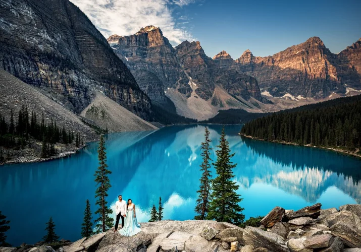 Banff Wedding Photography by Moraine Lake. Couple in love stand at edge of turquoise Lake with the view on huge Rocky Mountains.
