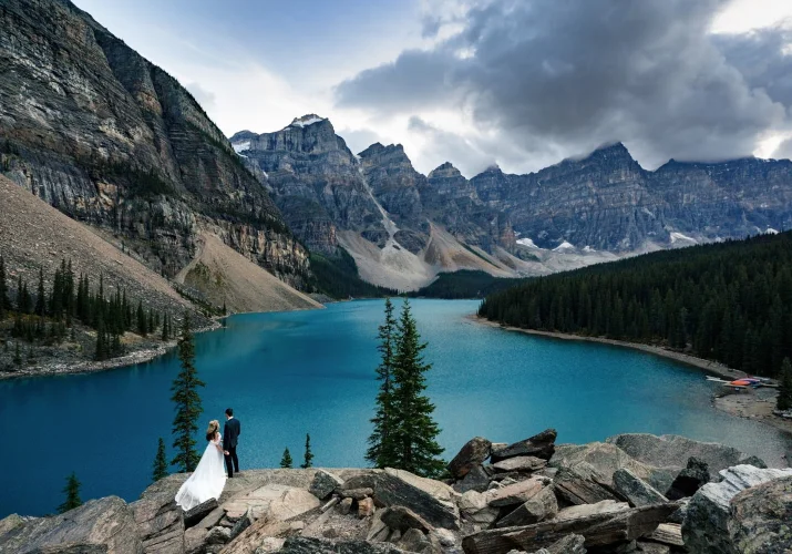 Cloudy morning at Moraine Lake during Mountain Weddings. Couple in love facing the lake end are fascinated with the blue lake and the power of the Rocky Mountains.