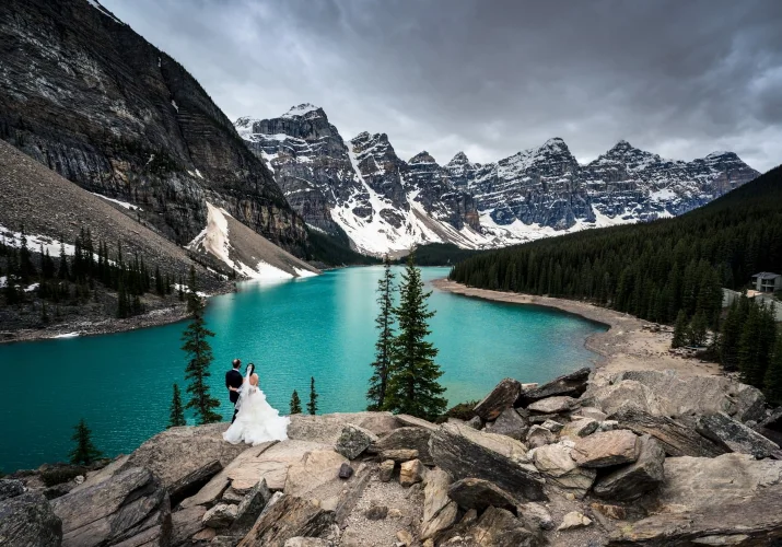 Banff Wedding Photography at Moraine Lake. Bride and groom stand in a hug watching magnificent turquoise c colour of the lake.