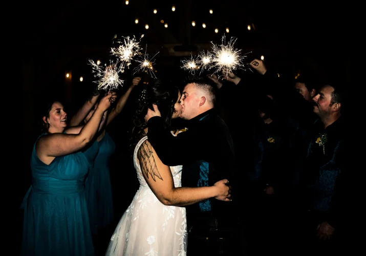 Newlyweds share a kiss while wedding party holds sparkles .