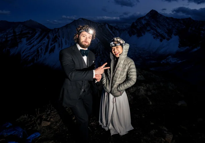Bride and groom on Hiking Adventure on their way back during ight. They wear headlamps on their heads.