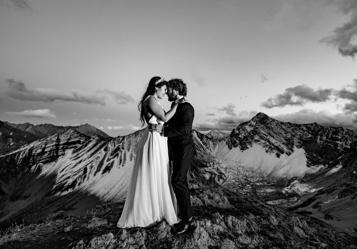 Bride and Groom facing each other on the top of the mountain during Mountain Weddings. Behind them huge mountains covered with snow.
