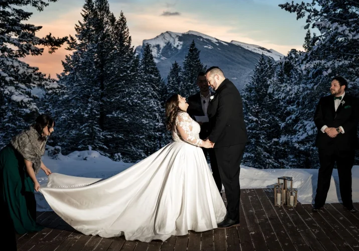 Amazing Banff Wedding Ceremony during winter time and sunset. Bride an groom hold their hands and look into each-others eyes.