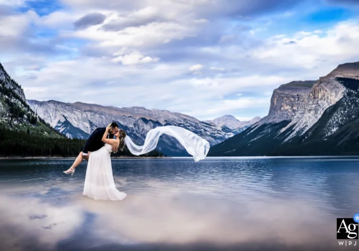 Newlyweds dance at Minnewanka Lake in Banff while her veil flies with the wind