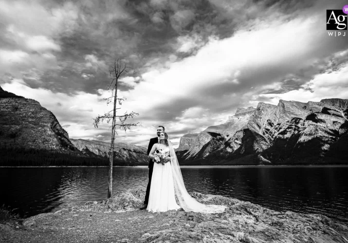Groom hugging his wife at Minnewanka Lake. Photo taken by best Banff Wedding Photographer in black and white.