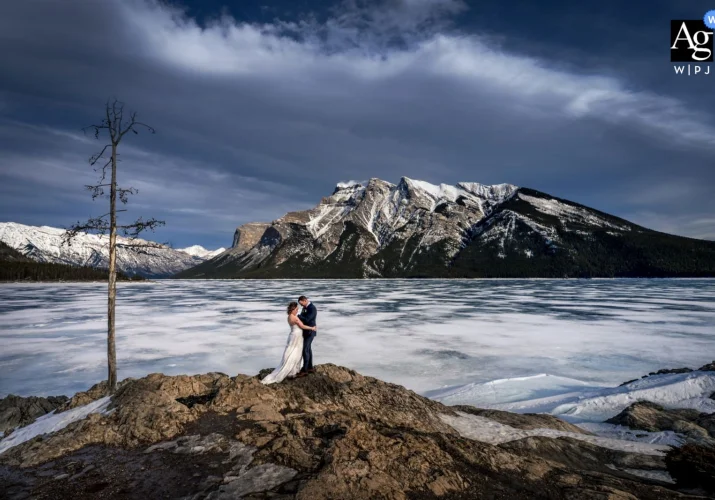 Winter Wedding Portrait Session takan by Banff Wedding Photographer of bride and groom in a hug at frozen Minnewanka Lake.
