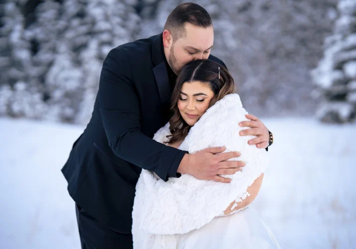 Groom holds his wife in the wintertime in Banff. He protects her from the cold.