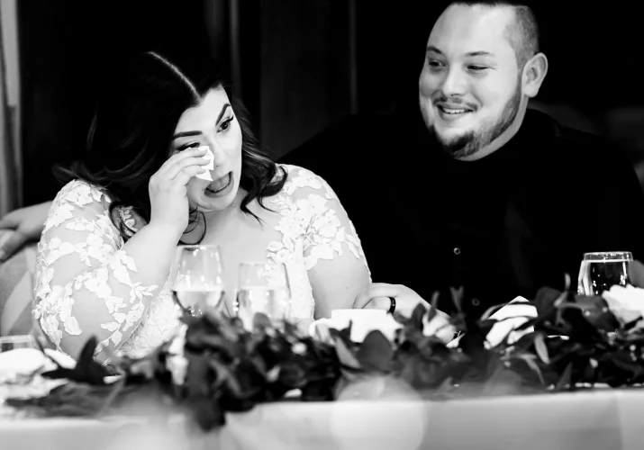 Bride wipes her tears with the napkin during the touching speeches while the groom look at her.