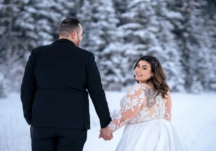 Bride and groom walk in Banff in the winter scenery when the bride look over the shoulder and smiles.